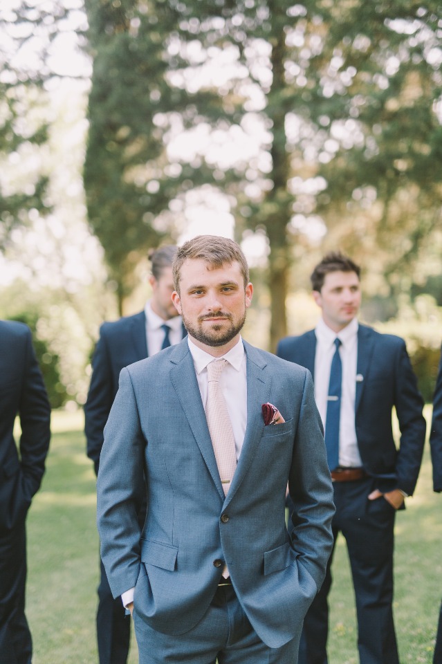Groom in blue suit with groomsmen in the background, outside