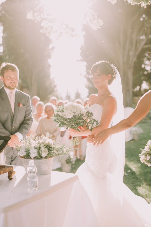 Bride holding flowers during a sunlit outdoor wedding ceremony