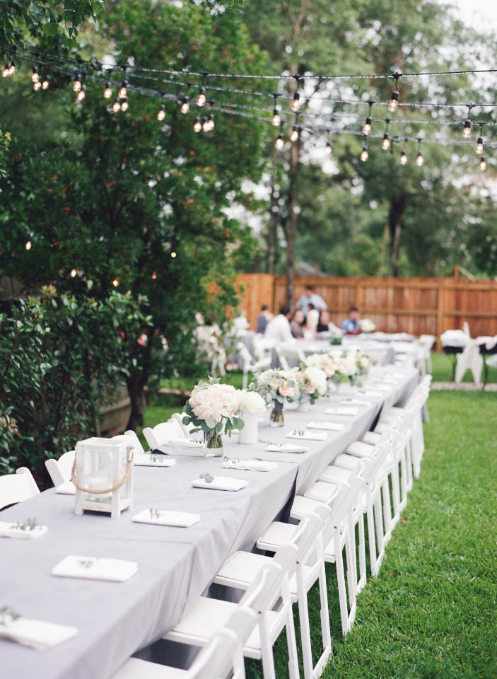 Long table set for outdoor event with string lights overhead
