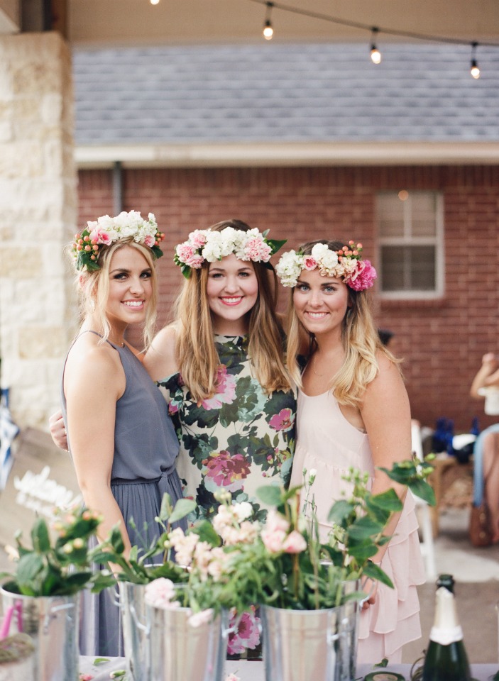 Three smiling women wearing flower crowns at a garden party