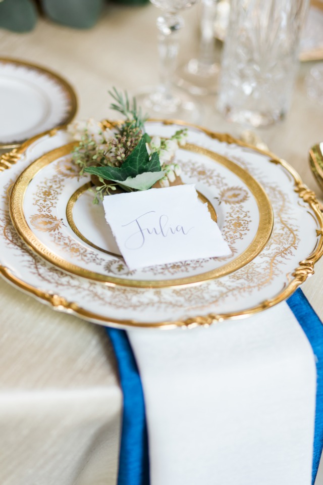 royal looking gold and white place setting with royal blue linen accent