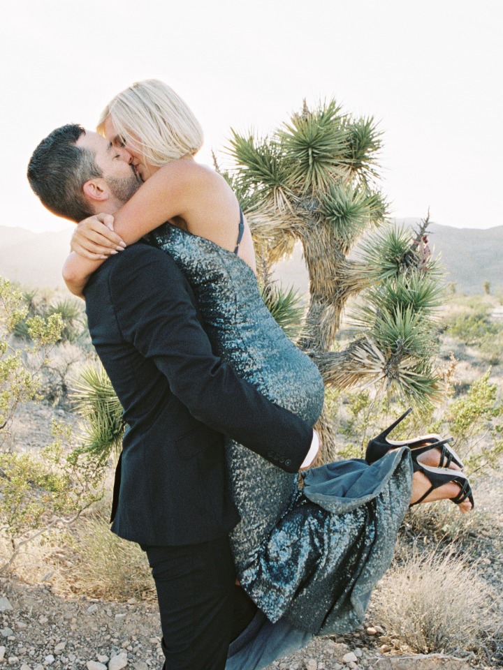Groom carries bride in a loving embrace with a desert background