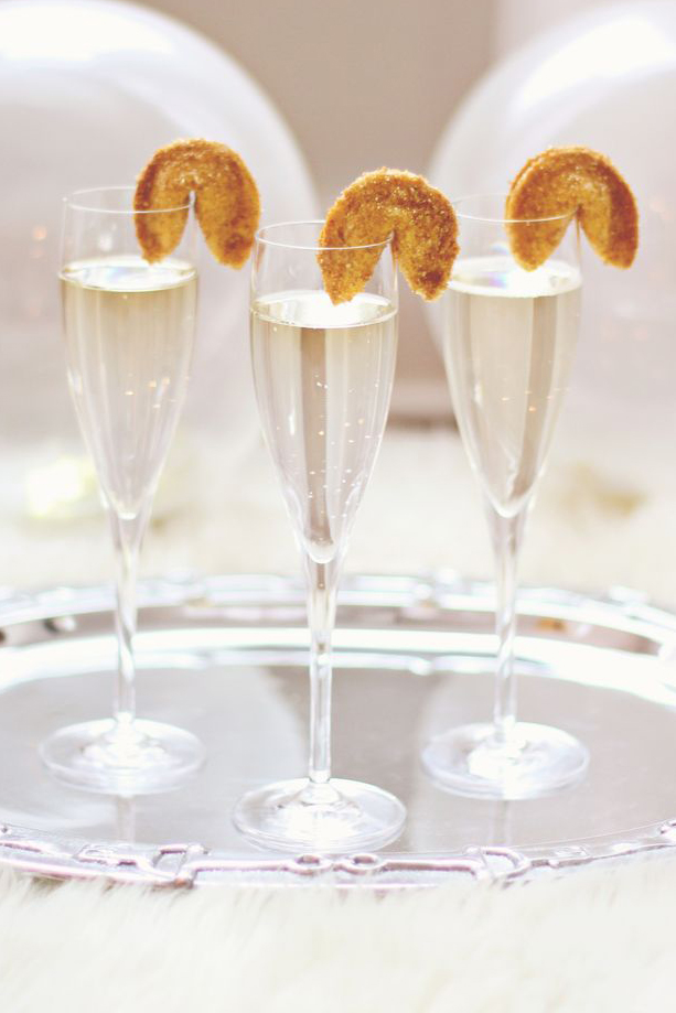 Three champagne flutes with fortune cookies on the rim