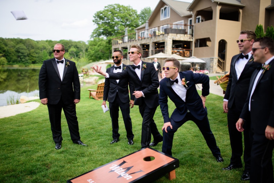 Groomsmen in tuxedos playing cornhole at wedding venue