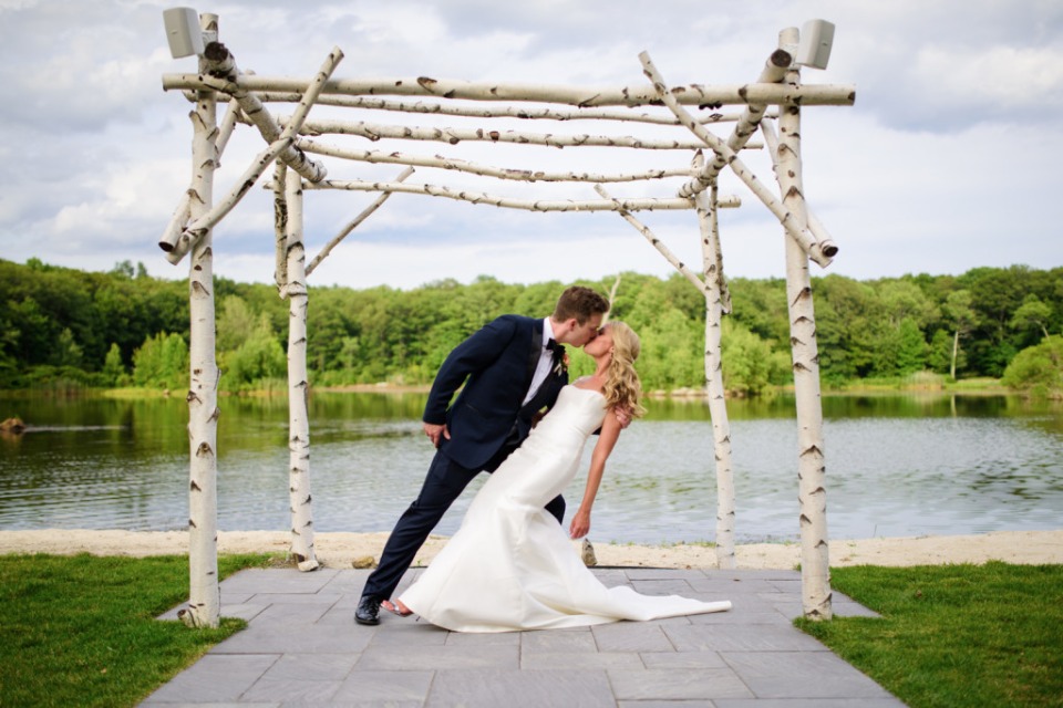 Bride and groom kissing under birch arbor near lake