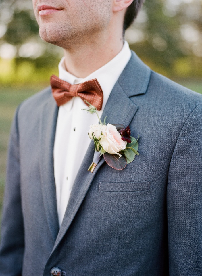 Groom in gray suit with a brown bow tie and boutonniere at wedding