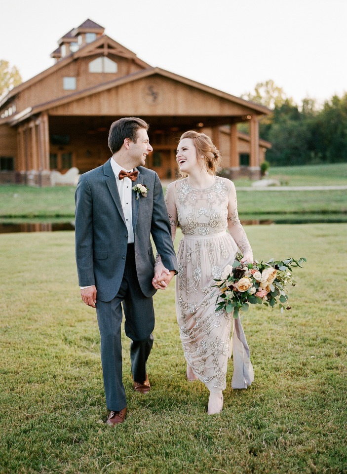 Newlyweds joyfully hold hands while walking on the grass