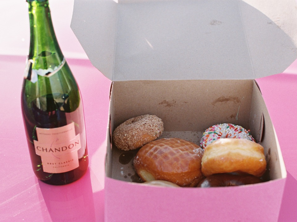 Box of donuts and bottle of Chandon sparkling wine on pink surface