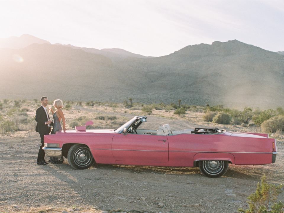 Couple in a pink convertible car enjoy desert sunset views