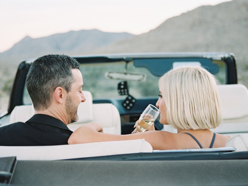 Couple in a convertible car toasting with champagne in desert landscape