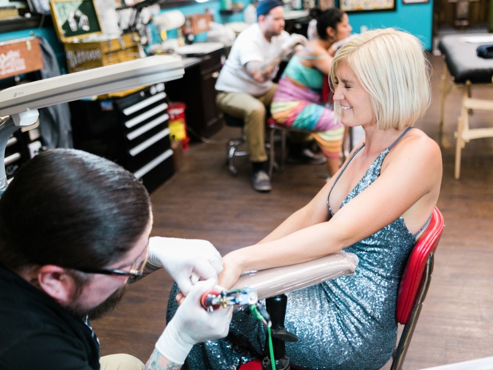Woman smiles as tattoo artist inks her arm in a studio
