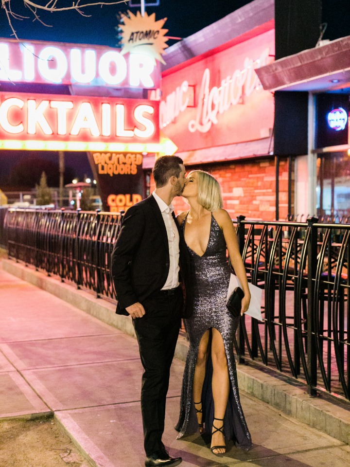 Couple kissing in front of a neon liquor sign at night
