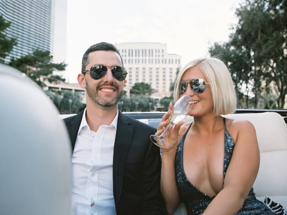 Smiling couple enjoying champagne in a convertible with city background