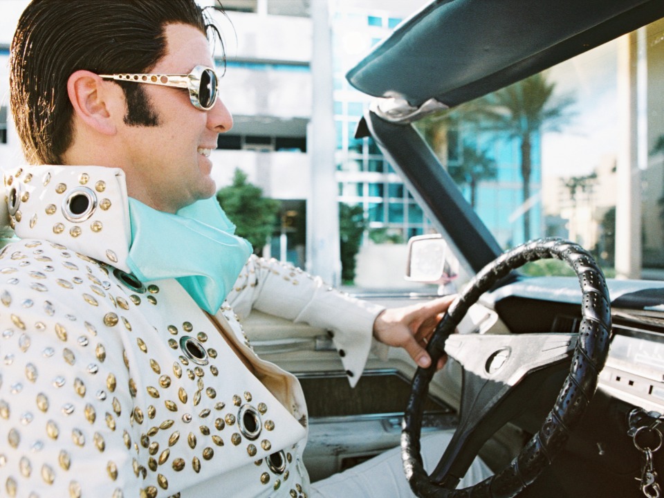 Elvis Presley impersonator in a white car driving down the road