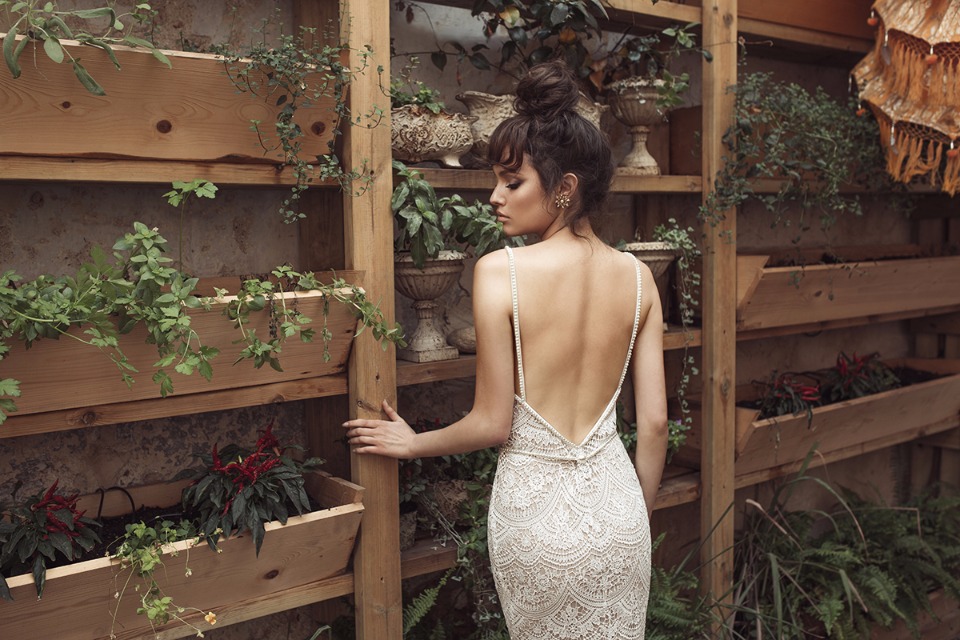 Elegant bride in backless dress near wooden plant shelves