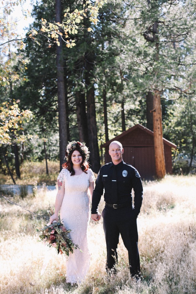 Bride and policeman groom holding hands at forest wedding