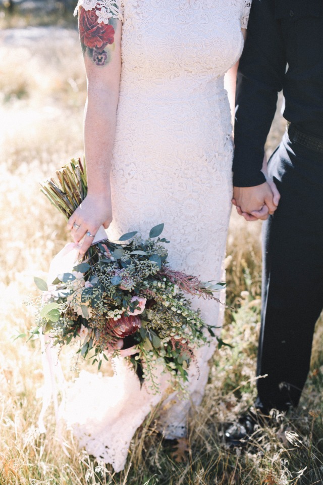 Bride with tattoo and floral bouquet holding hands