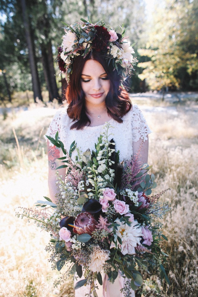 Bride with floral crown holding a large bouquet outdoors