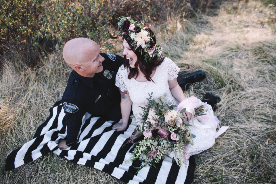 Bride and policeman groom laugh on a blanket outdoors