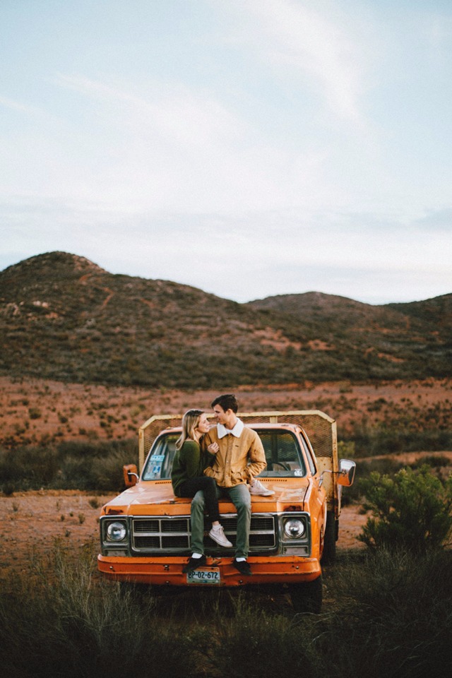 Couple cuddling on vintage truck in mountains