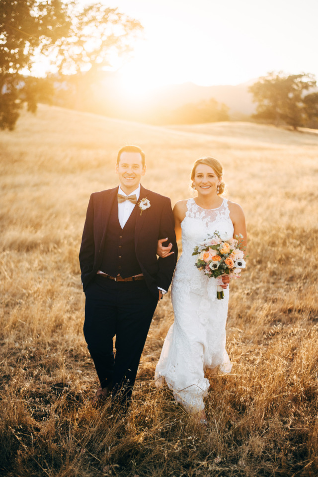 Happy couple walking in a field during their wedding day at sunset