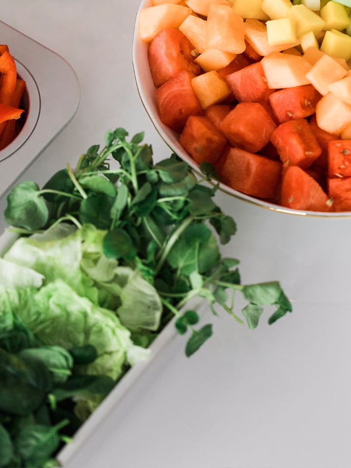 Colorful fruit salad and fresh greens on a white surface