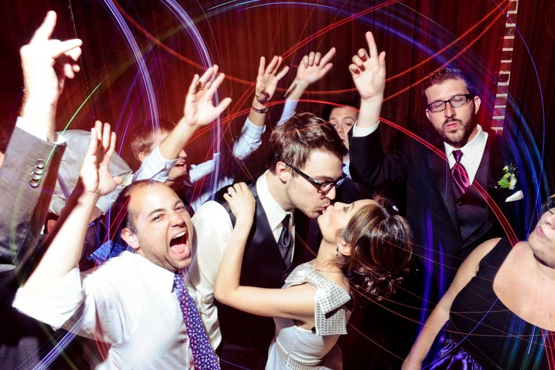 Happy wedding party with dancing guests and a kiss