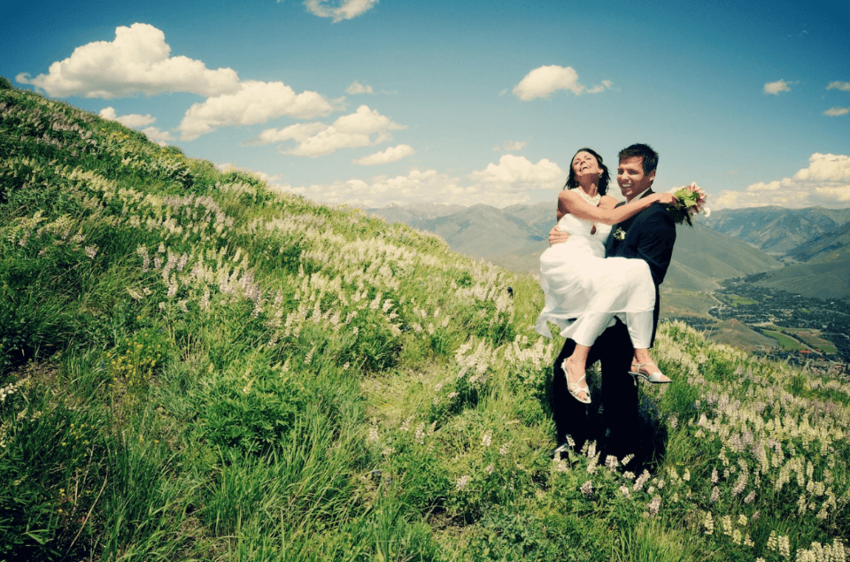 Groom carries bride joyfully on a mountaintop after their wedding
