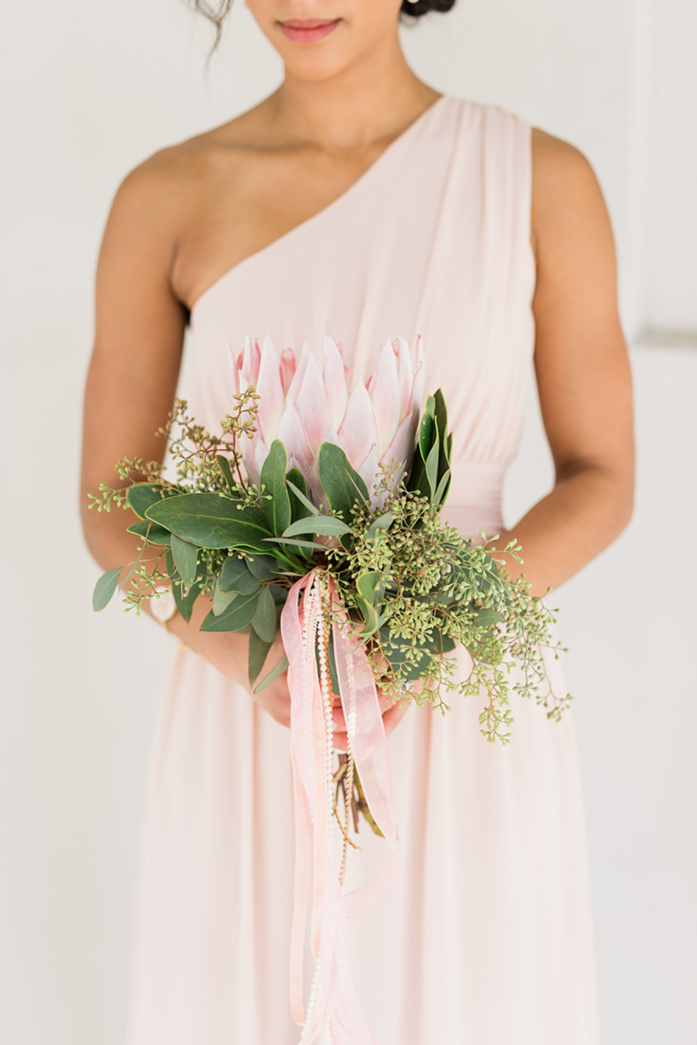 one shoulder blush bridesmaids dress with protea bouquet