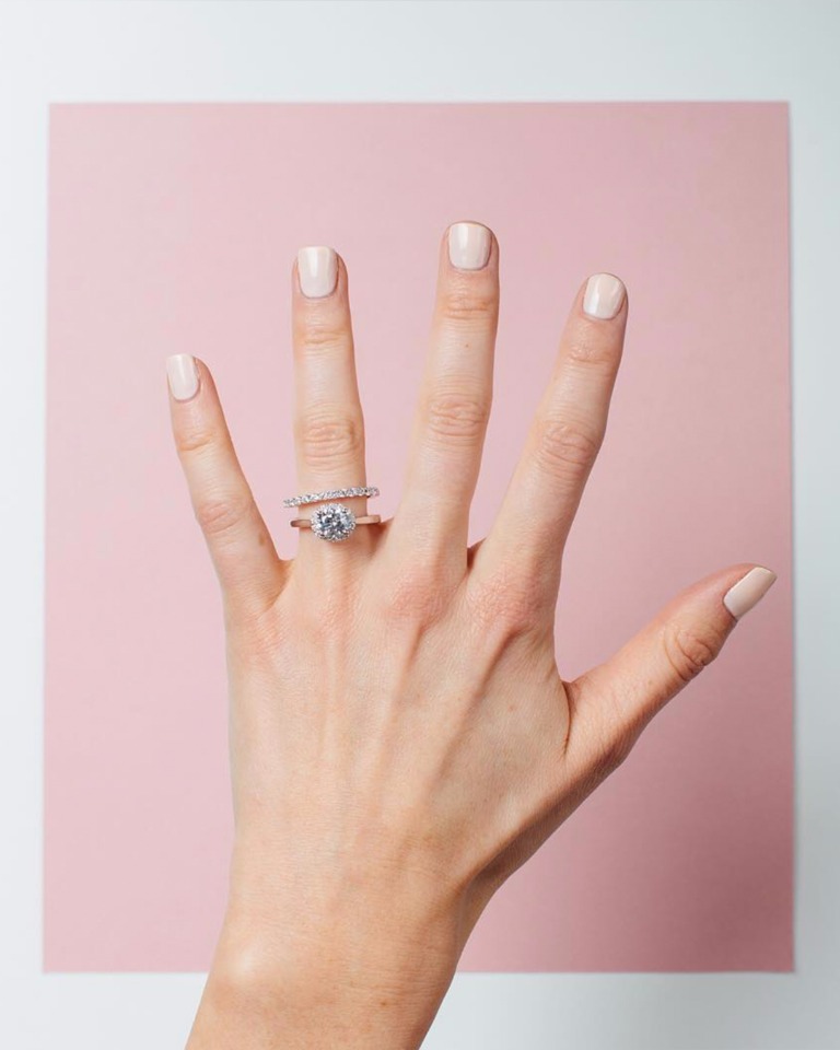 Engagement ring on woman's hand with pink background