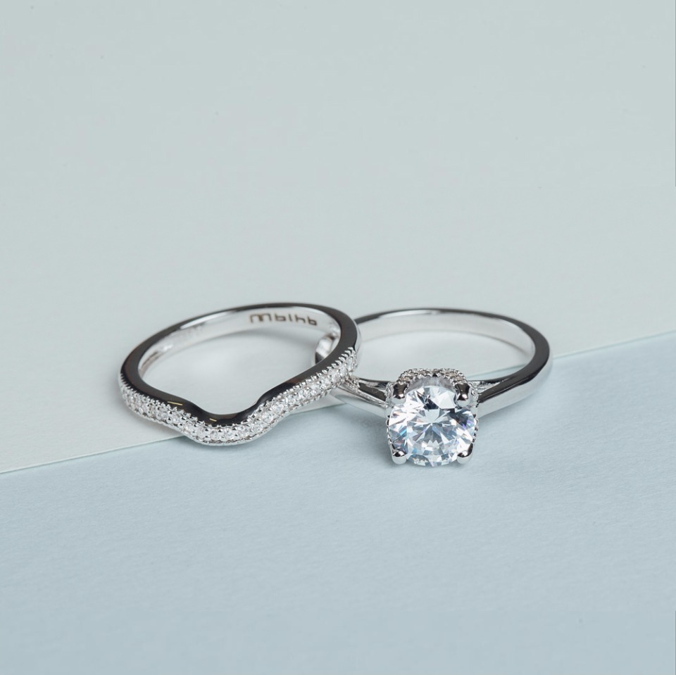 Silver engagement and wedding ring set on blue surface