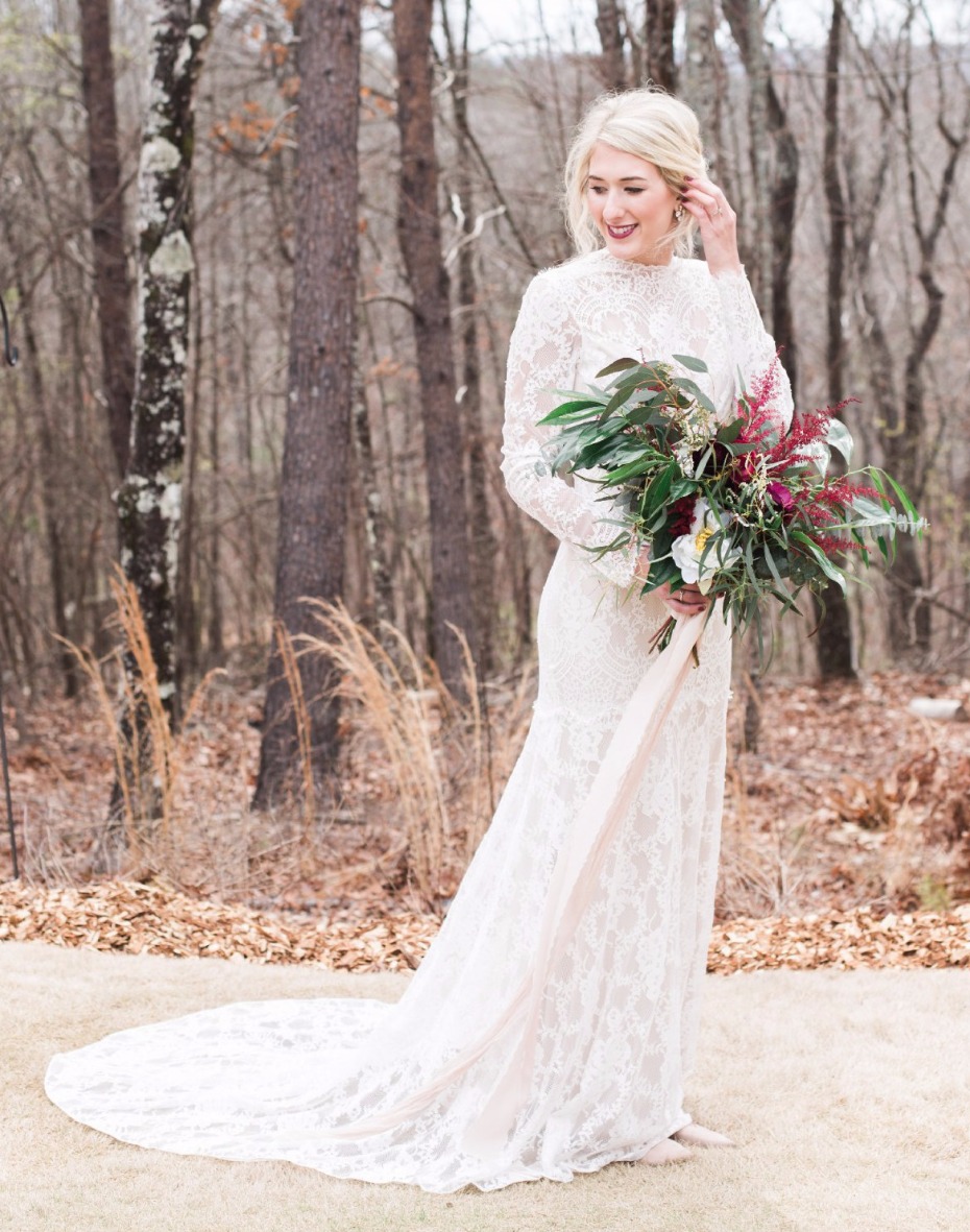 Elegant bride in lace gown holds floral bouquet outdoors