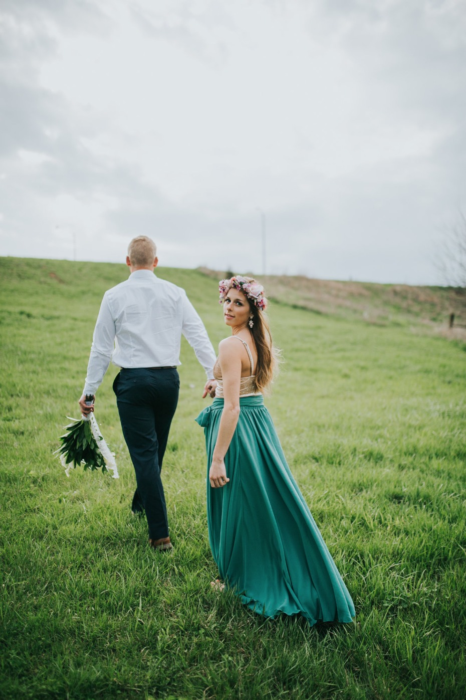 Couple walks through field bride looks back at camera