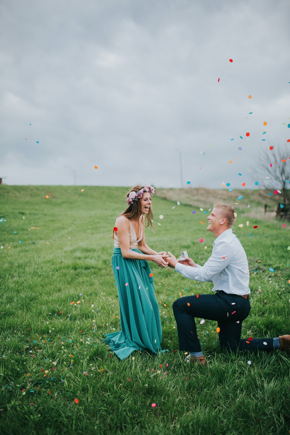 Man proposing to woman in field with confetti rain