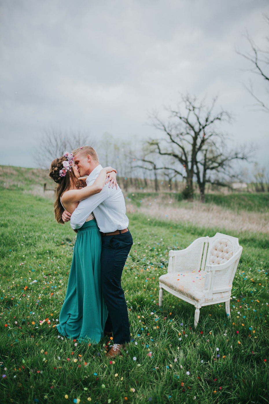 Couple kissing in meadow with flower crown and vintage chair