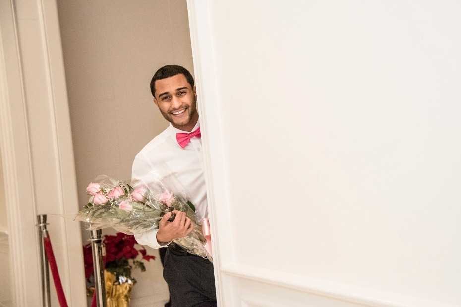 Man with roses and pink bow tie peeking through doorway