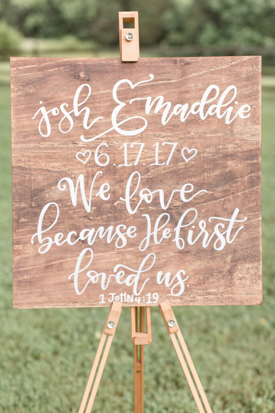 wooden sign with calligraphy Bible verse on it. We love because he first loved us - 1 John 4:19
