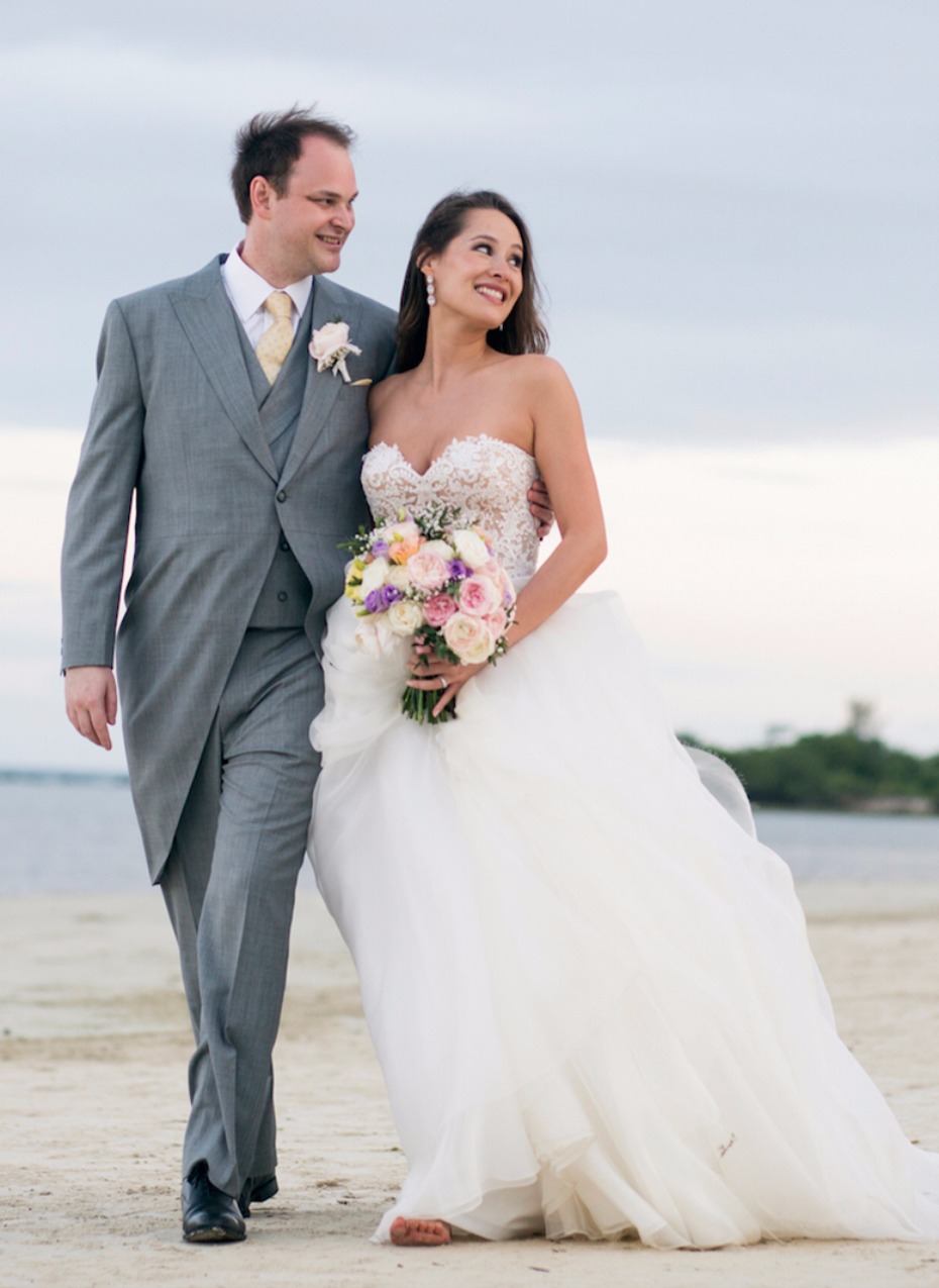Newlyweds walk barefoot on a sandy beach after wedding