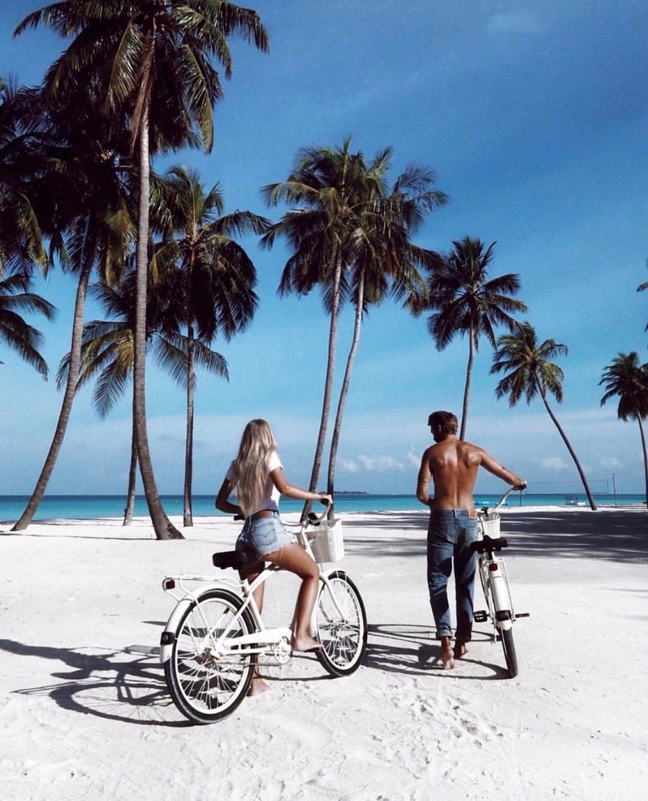 Couple biking on a white sand beach with palm trees