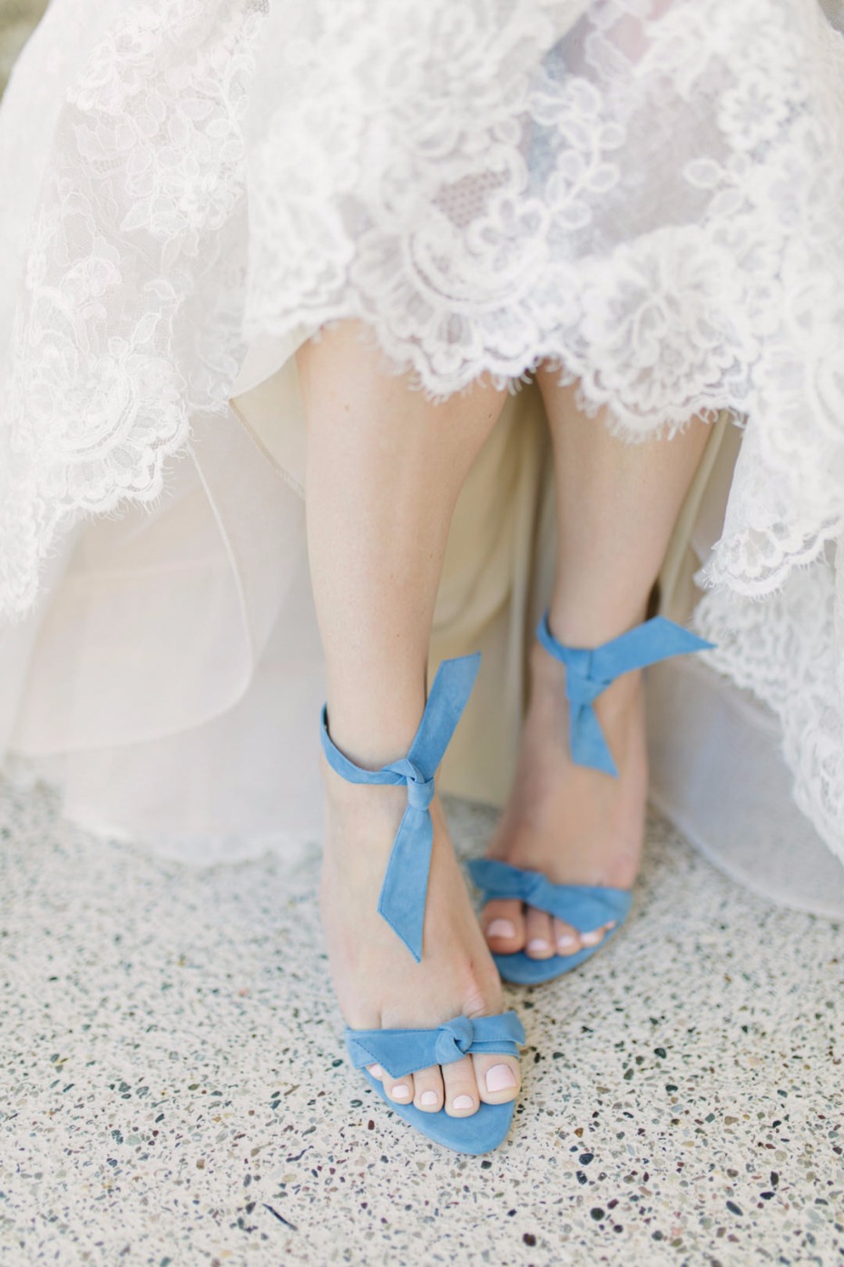 Elegant blue wedding shoes peeking under a white lace dress