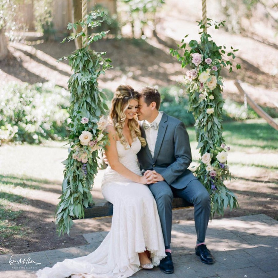 Newlyweds on floral wedding swing in garden setting