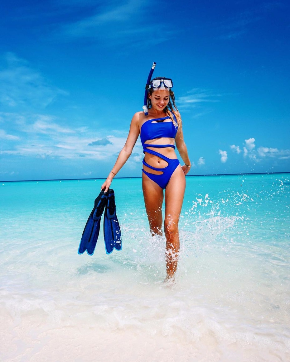 Woman in blue swimsuit with snorkel and flippers on beach