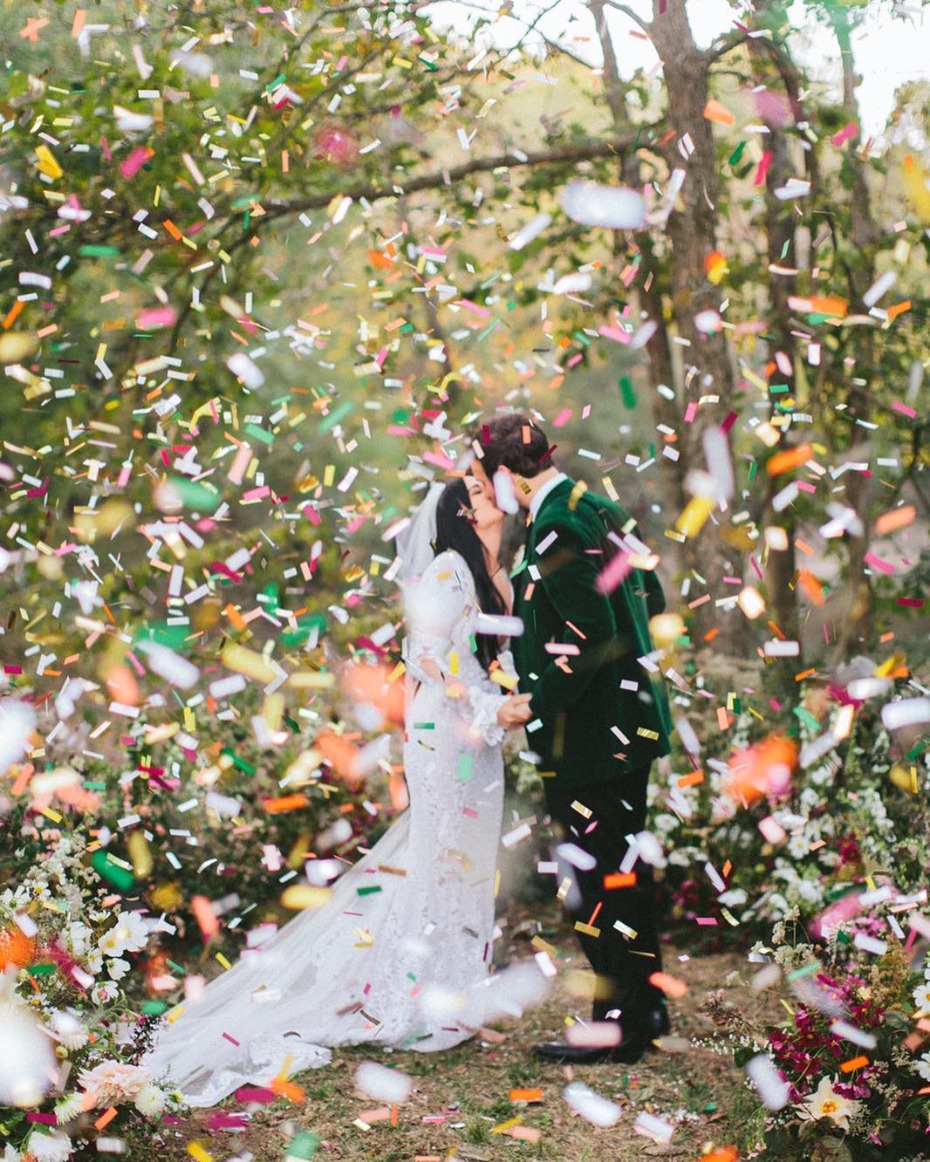Bride and groom kiss in confetti at forest wedding