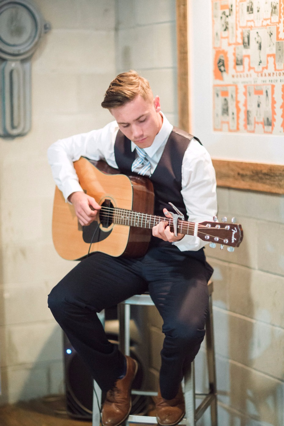 Young man playing acoustic guitar indoors on a stool