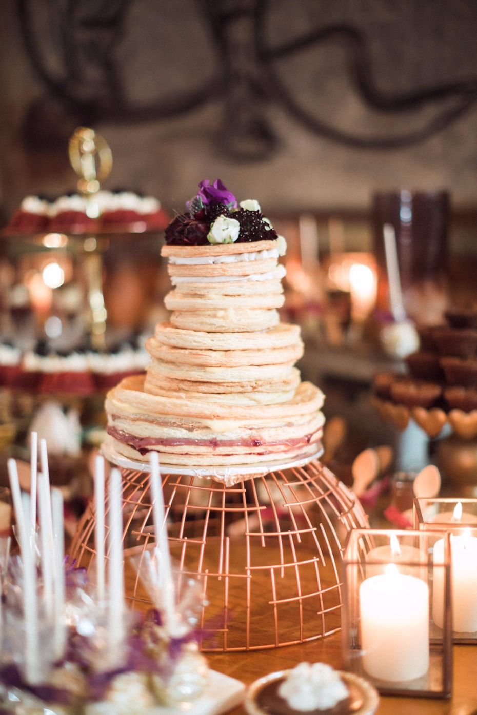 A tiered dessert cake with berries, on a copper wire display