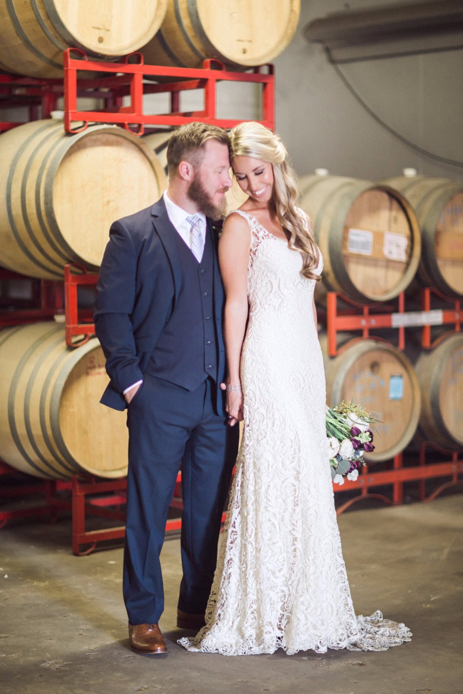 Bride and groom pose in front of wine barrels on wedding day