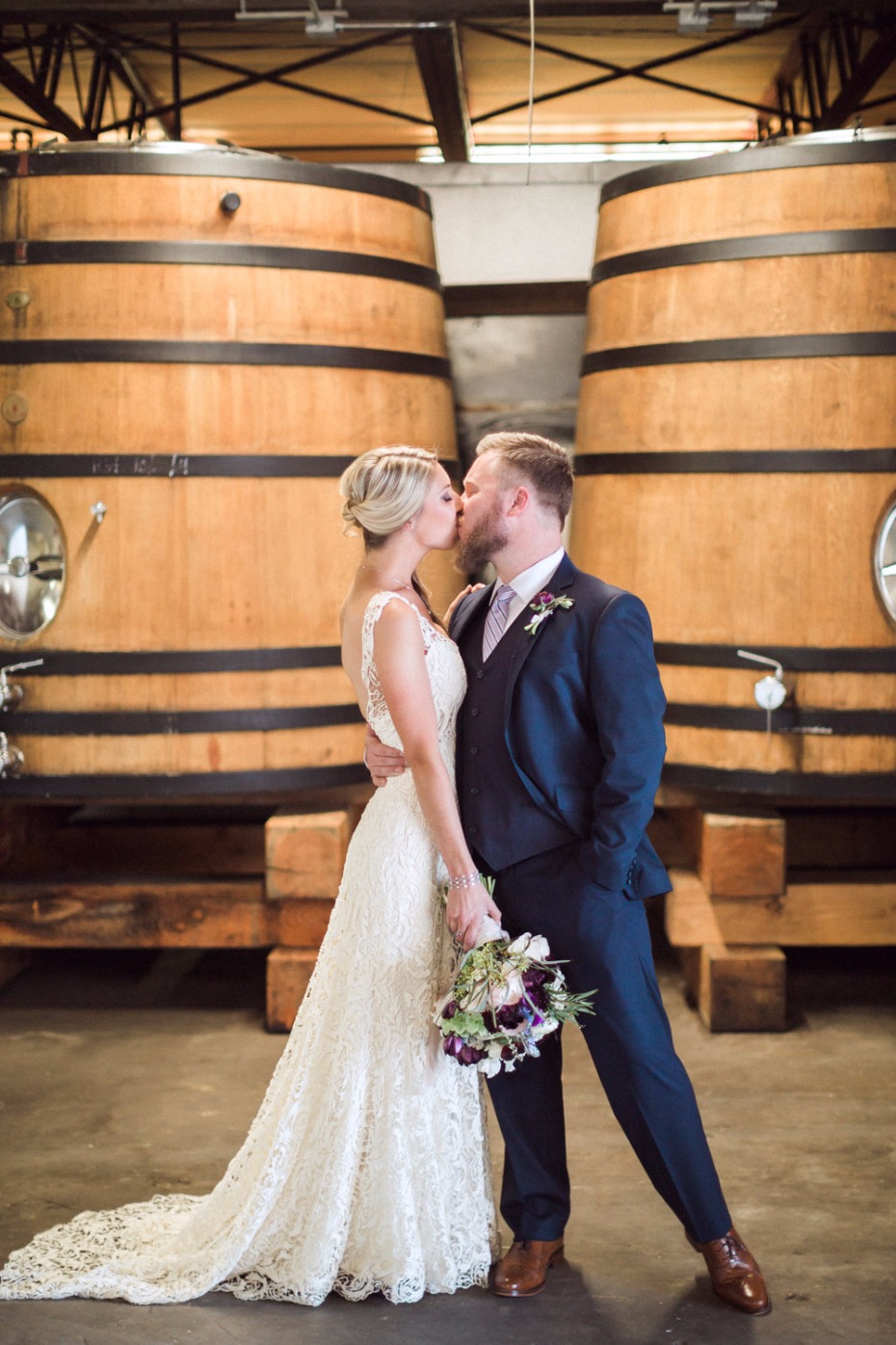 Bride and groom kiss by wine barrels wedding portrait