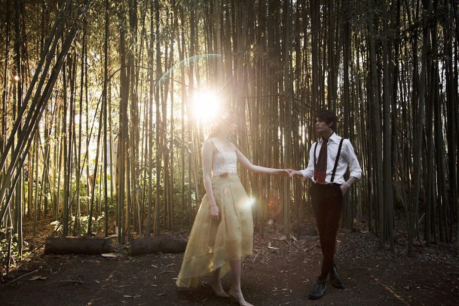 Couple holding hands in a bamboo forest with bright sunlight