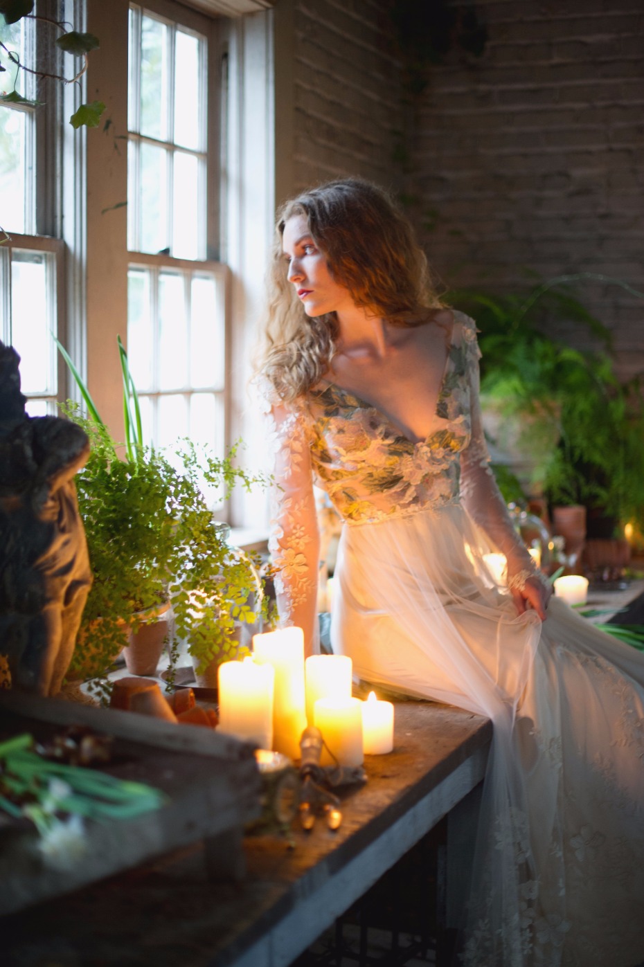 Woman in ethereal dress surrounded by plants and candles