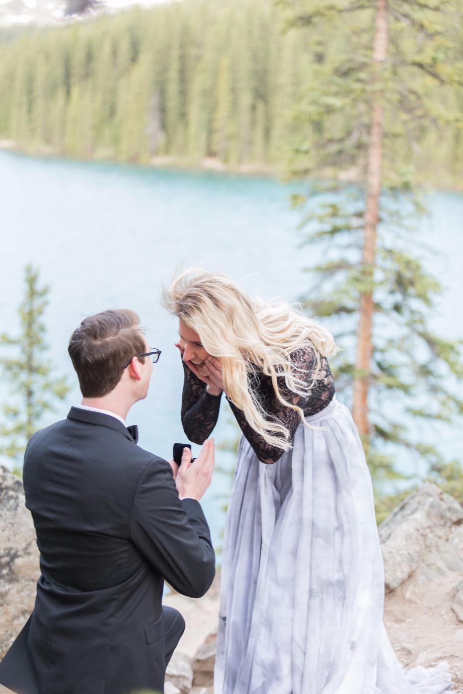 Man proposing to a surprised woman outdoors near a lake
